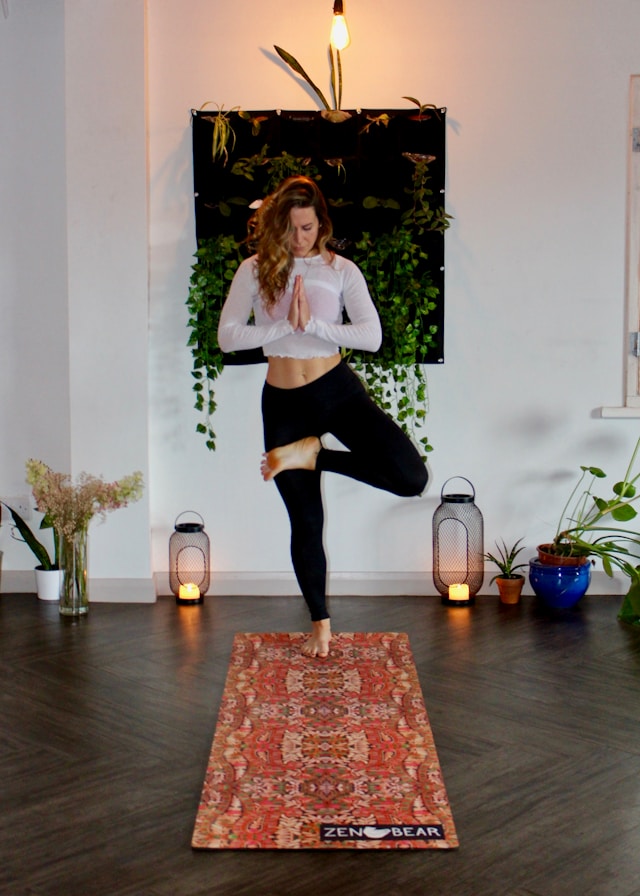 image shows woman doing yoga at home she is standing on her yoga mat blog post is about how to start a home yoga or self yoga practice