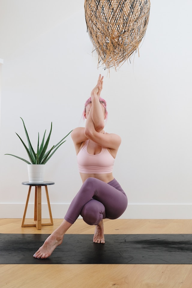 image shows a woman doing yoga at home she is doing an eagle pose variation blog post is about starting a yoga practice at home