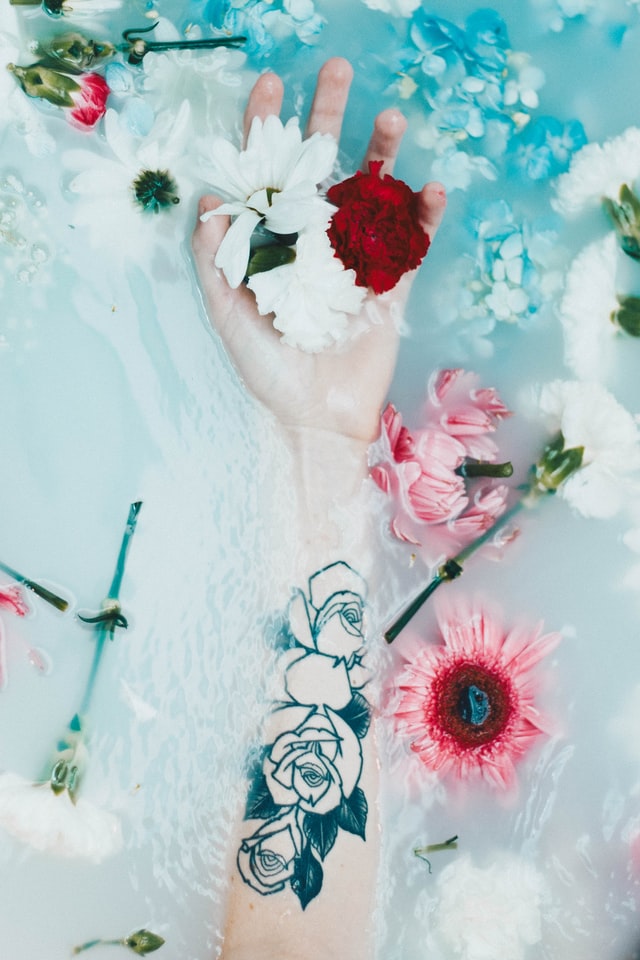 relaxing bath with flowers floating showing arm with rose tattoo
