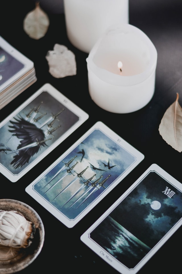 tarot cards lined up on black table with white candle burning learn how to develop a full moon ritual