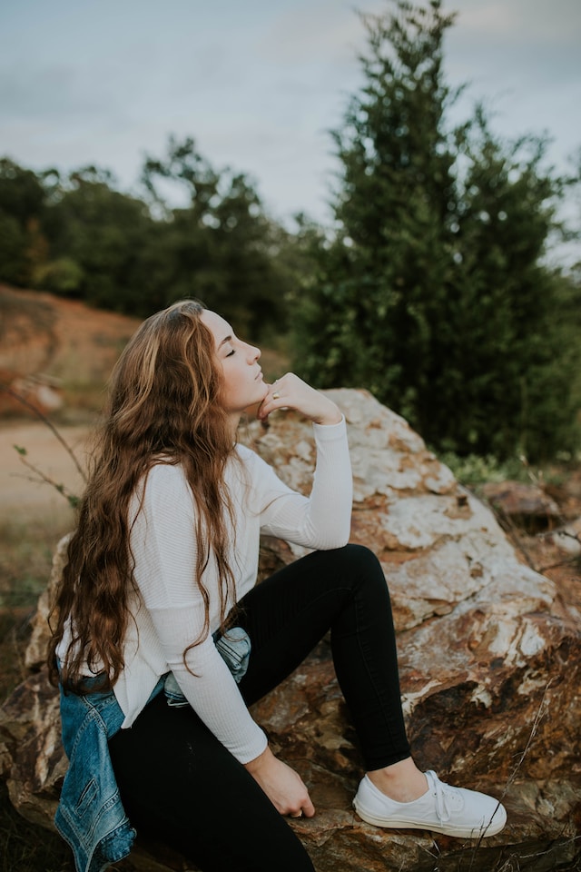 picture showing woman with black jeans and white sweater sitting in nature enjoying a moment of calm best Sunday routine practice mindfulness