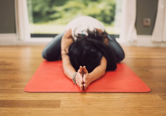 picture showing young woman with dark hair on red yoga mat in child's pose in home yoga space