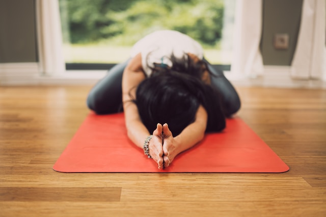 picture showing young woman with dark hair on red yoga mat in child's pose in home yoga space