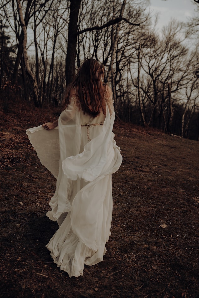 woman wearing white dress walking through forrest woman shown from the back