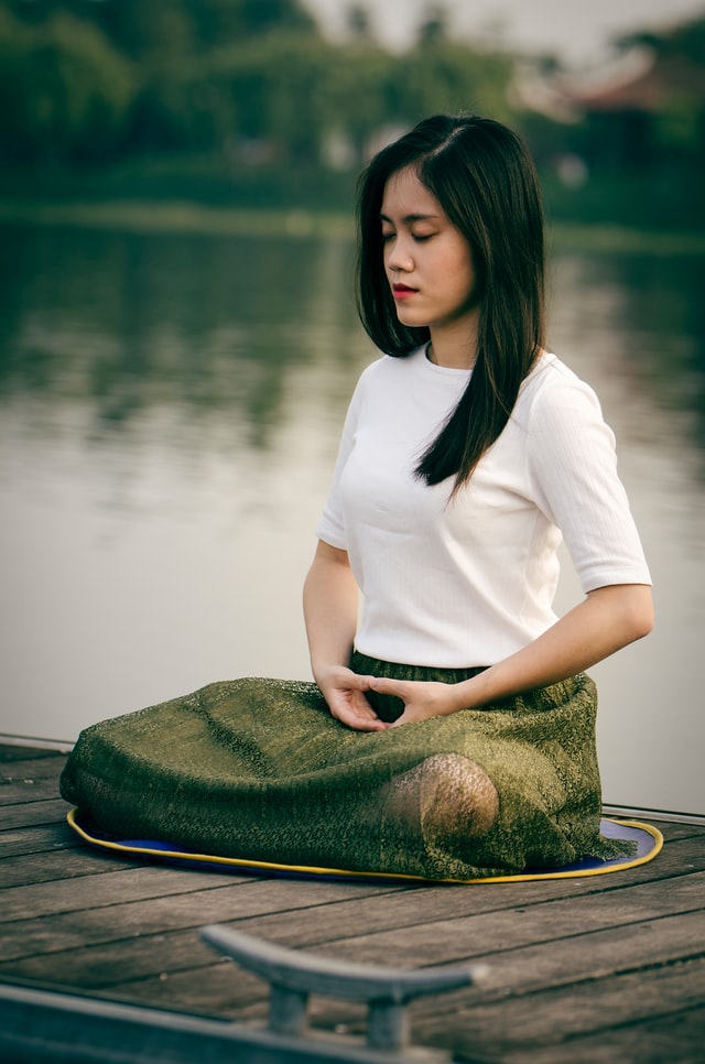 young woman meditating next to lake yoga for grief