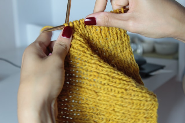 close up of woman hands with red painted finger nails knitting yellow scarf 12 self-care ideas for winter