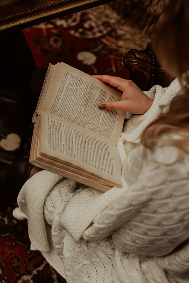 woman wearing white knitted jumper sitting in home environment reading a book 12 self-care ideas for winter