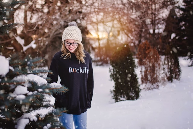the picture shows a woman dressed in jeans and a pullover wearing a winter hat in an outside setting with snow and the blog post is about winter self care tips