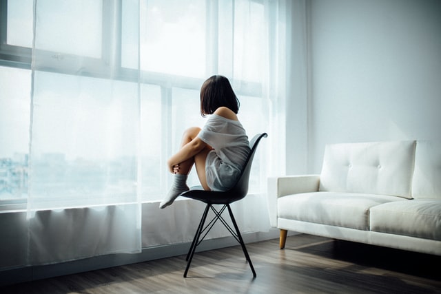 young woman sitting on chair looking out of window mental health