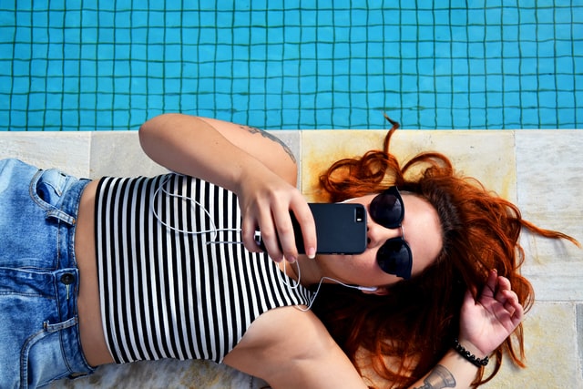 woman with red hair lying next to pool listening to music