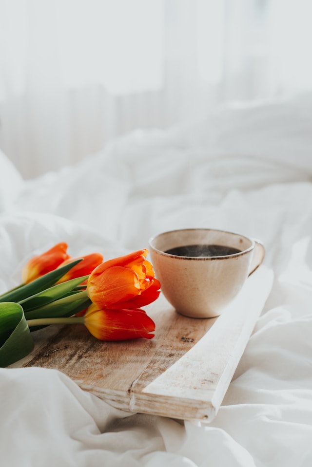 the picture shows a close up of a cup of coffee and a bunch of orange tulips on a white surface and the blog post is about wellness tips for spring
