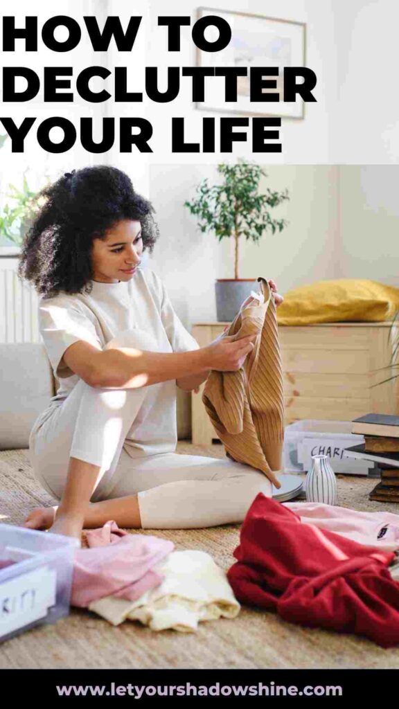 woman sitting on floor in her living room sorting clothing how to declutter your life