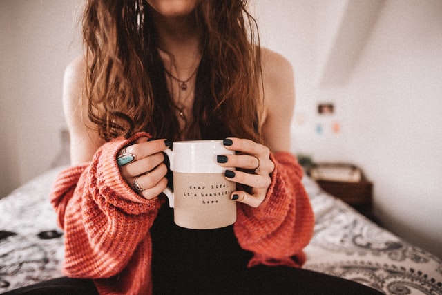 women with long brown hair sitting on bed drinking morning coffee 5 ways to practice gratitude daily