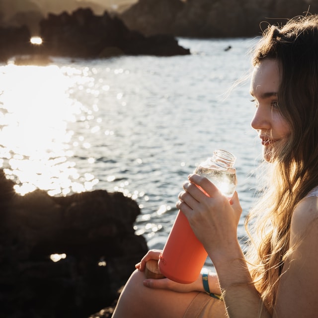 woman sitting at lake drinking out of water bottle 10 healthy lifestyle habits hydrate