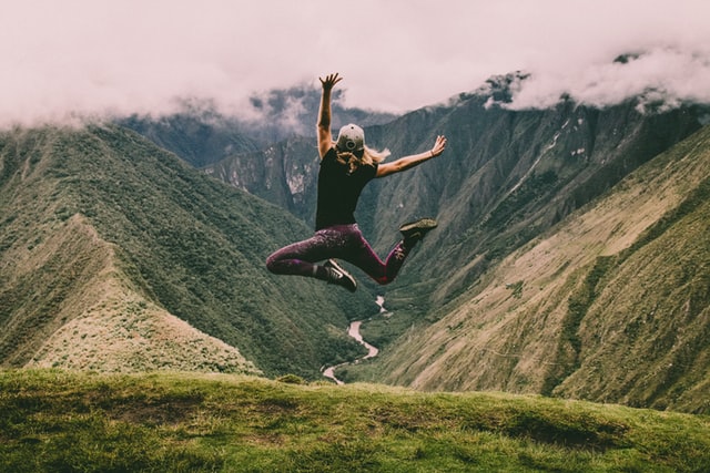 woman jumping up in the air overlooking mountains happiness 10 healthy lifestyle habits