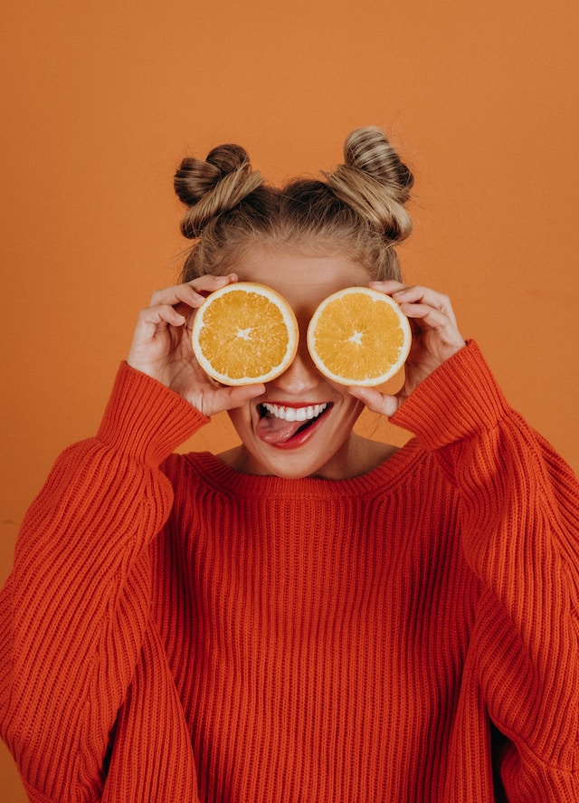picture showing woman wearing red jumper holding half an orange in front of each eye healthy lifestyle habits for busy women
