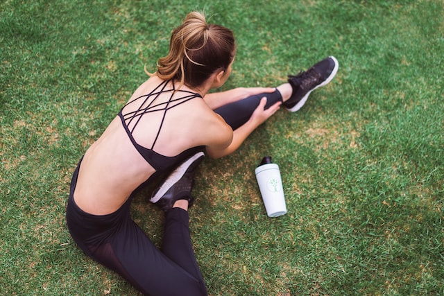 image showing woman sitting on grass stretching dressed in black sports gear healthy lifestyle habits