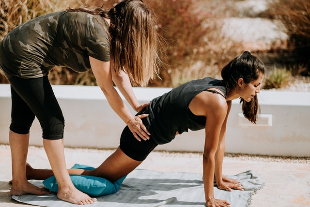 female yoga teacher giving adjust to yoga student in lizard pose 11 reasons why you should start yoga