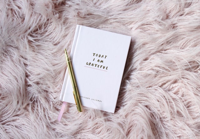 light pink gratitude journal placed on fluffy pink carpet with golden pen 11 reasons why you should start yoga practice gratitude