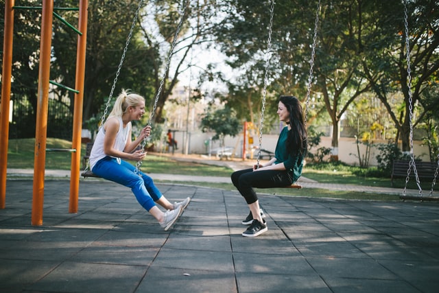 two women sitting on a swing each in the park 11 reasons why you should start yoga say goodbye to toxic environments