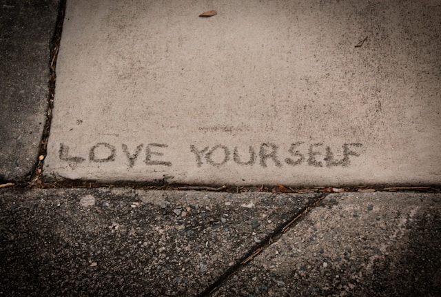 the picture shows a close up of a pavement and it says love yourself written on the pavement ,the blog post is about benefits of yoga and this part talks about cultivating self love