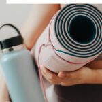 pinterest pin image showing a close up of a woman holding a yoga mat and a reusable water bottle blog post is about 20 benefits of yoga