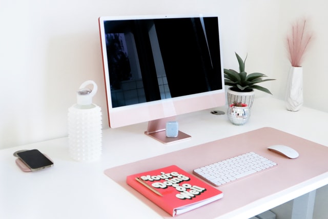 clean desk space in white and pink colours with laptop, keyboard and iphone how to practice self-care at work