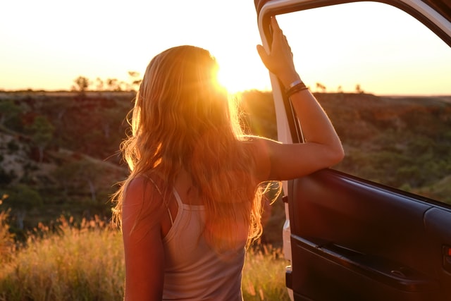 woman looking at sunset standing at car 12 self-care ideas for summer road trip