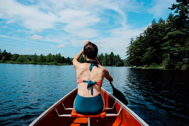 woman in boat on lake wearing bikini rowing 12 self-care ideas for summer