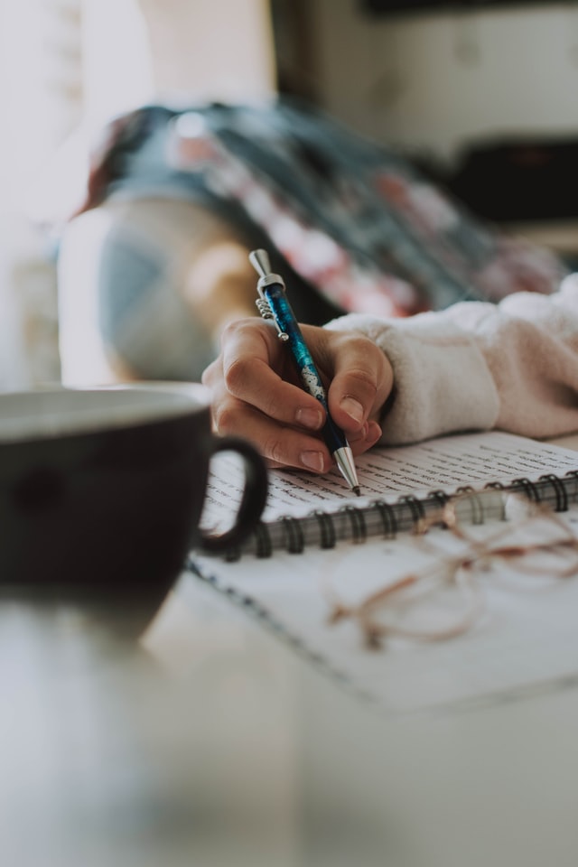 woman writing into notebook coffee cup standing next to notebook 7 tips on how to find a yoga retreat that is right for you