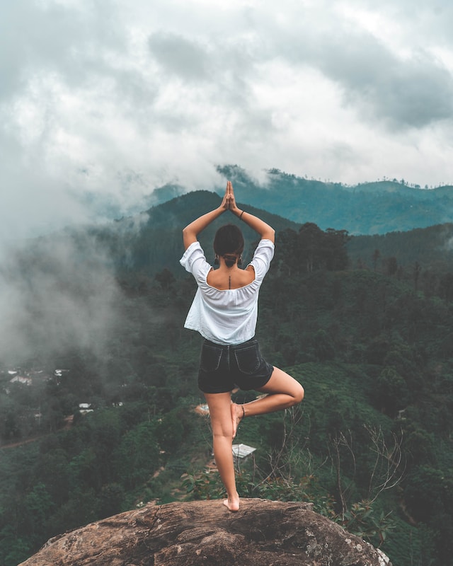 image showing woman standing on top of a mountain doing tree yoga pose how to choose a yoga retreat that is right for you