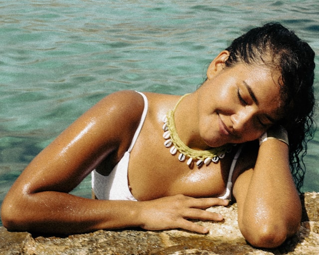 the picture shows a young woman posing in the water in front of the camera she is enjoying the summer sun; the blog post is about summer self-care ideas