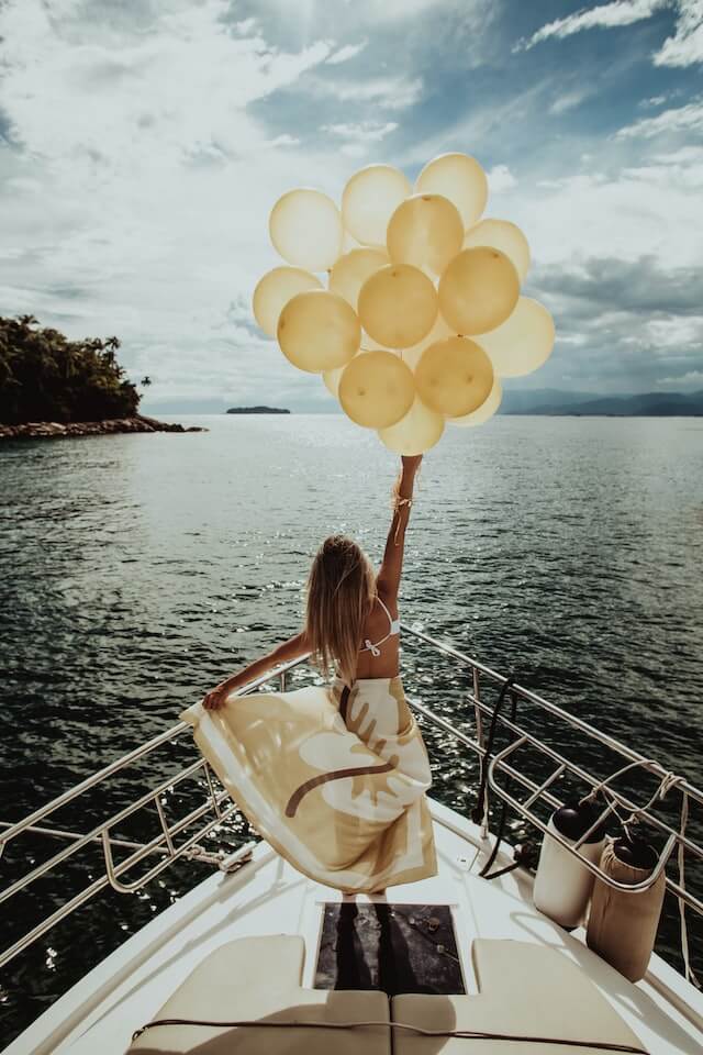 blonde haired woman standing on yard with back turned into camera holding yellow golden balloons in her right hand 13 feel-good things to do appreciate how far you have come
