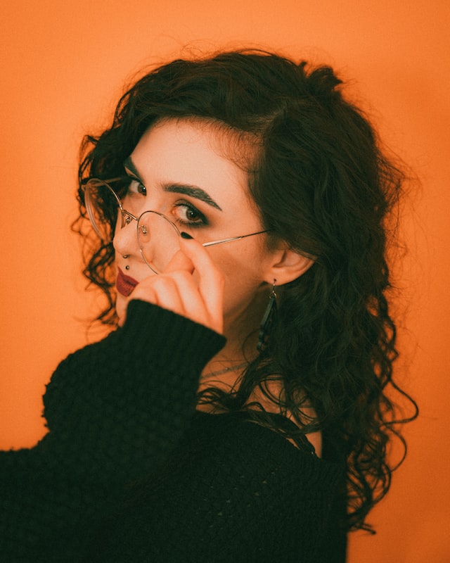 woman with dark curly hair and black sweater throwing a cheeky look into the camera 13 feel-good things to do have a little flirt