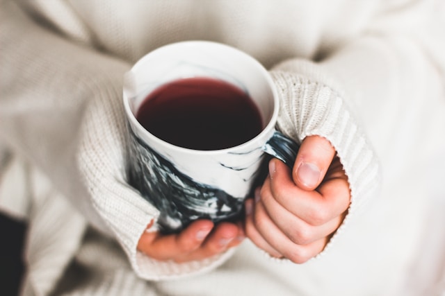 image is showing a close up of female hands holding a cup of tea woman is wearing a white wool sweater blog post is about crafting an evening routine