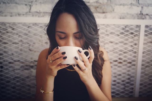 image showing a woman with dark hair holding and drinking a cup of tea blog post is about establishing an evening routine