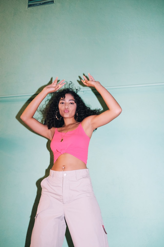 woman with curly dark hair and pink crop top and baggy trousers dancing feel good activities