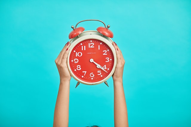 female hands holding up red and white vintage alarm clock in front of turquoise background 