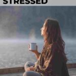 woman sitting on pier at a lake enjoying a cup of coffee 11 easy ways to relax when stressed