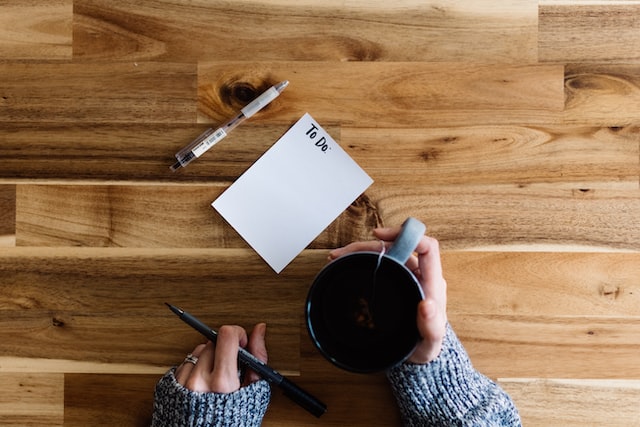 close up of a to-do list on wooden table showing to-do list, woman hands holding a cup of coffee 11 easy ways to relax when stressed make a to-do list