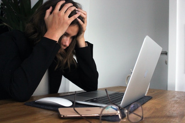 woman sitting in front of laptop with arms over her head feeling exhausted toxic habits to quit leaving things to the last minute