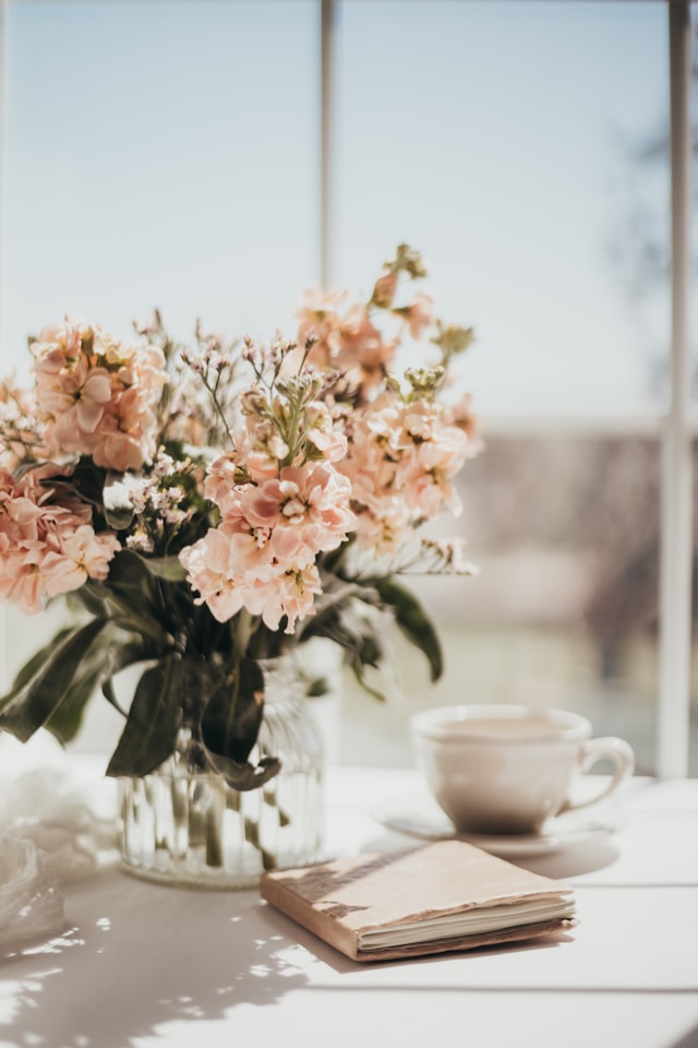 the picture shows a close up of a table with a beautiful bunch of flowers, a cup of coffee and a closed journal the blog post is about glow up tips and how to glow up mentally and physically