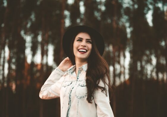 picture showing a woman with dark hair wearing a black hat woman is smiling and in nature setting blog post is about mindful glow up tips