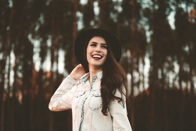 picture showing a woman with dark hair wearing a black hat woman is smiling and in nature setting blog post is about mindful glow up tips