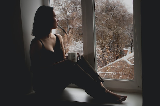 image showing woman sitting inside a room looking out of the window coping with the holidays