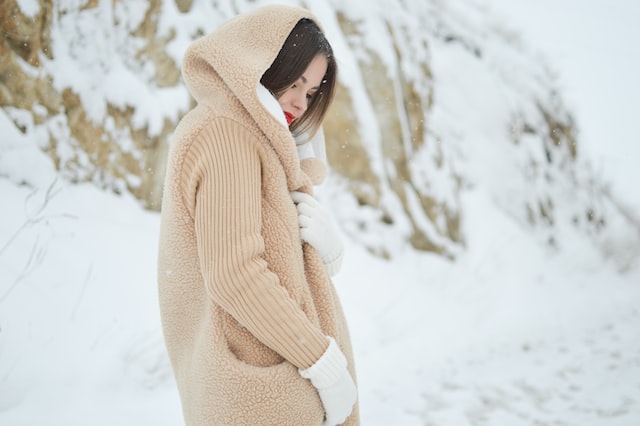 woman dressed in light beige coat walking in winter landscape setting how to best deal with holiday stress connect with nature