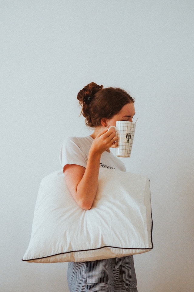picture showing woman from side view holding pillow under her right arm and coffee cup in her right hand 5 steps to start a healthy lifestyle 