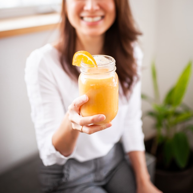 the picture shows a woman blended out of the image and she is holding a glass of fresh orange juice in her hand and into the camera; the blog post is about how to live a healthy lifestyle and 5 steps to a healthy lifestyle
