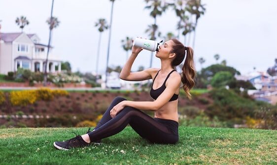 woman in sports outfit sitting on green grass drinking water post workout session how to start a healthy lifestyle and stick with it