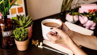 close up of female hands holding coffee cup with coffee and journal on brown desk how to start journaling